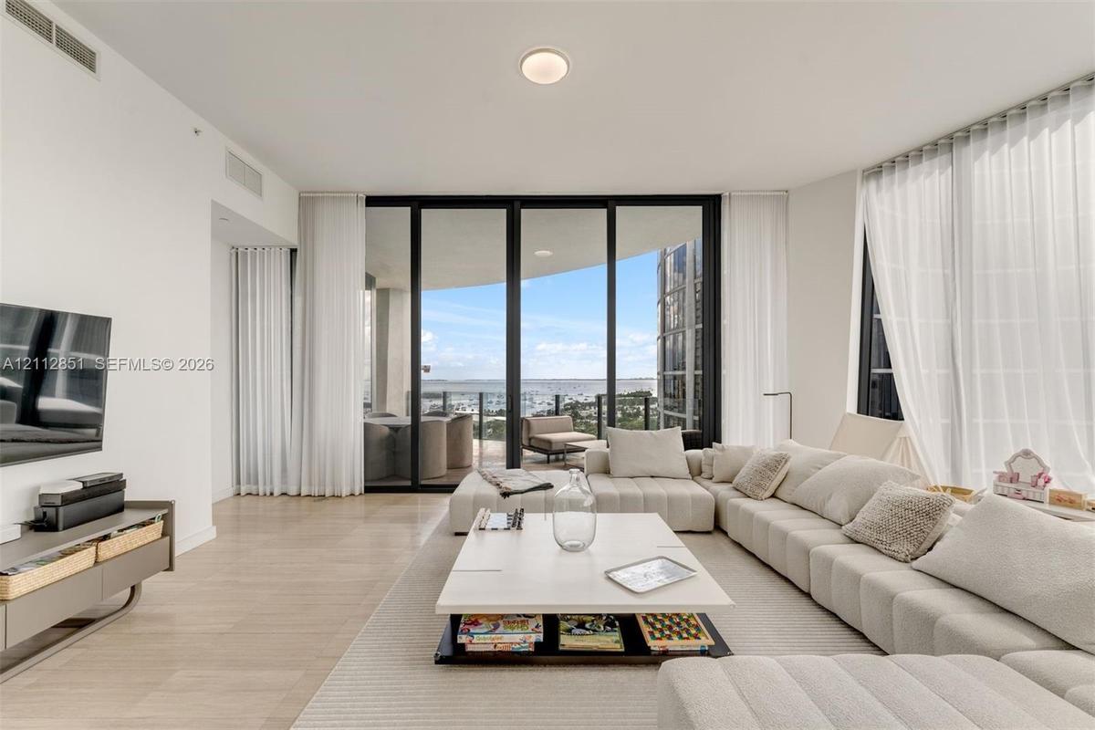 Living area featuring floor-to-ceiling glass sliding doors, neutral tile flooring, and integrated ceiling lighting