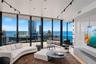 Floor-to-ceiling windows featuring panoramic water and city scenery, expansive curved balcony, stone-finish accent wall with integrated media cabinetr