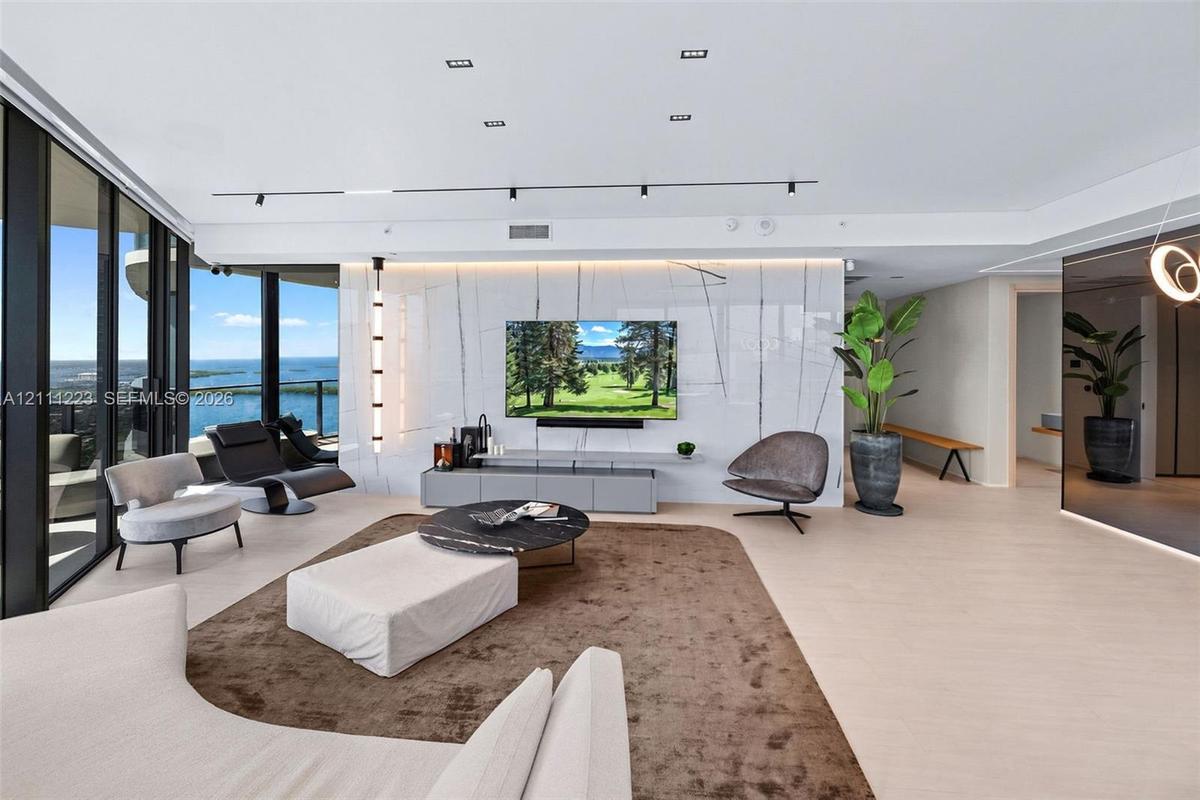 Floor-to-ceiling glass wall, large-format stone-finish feature wall, recessed ceiling lighting, track lighting, and light-tone wood-finish flooring