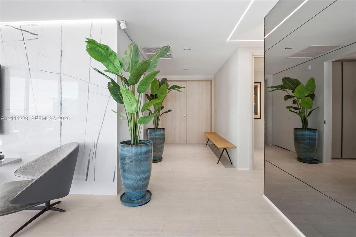 Large-format stone-style wall cladding with neutral veining, high-gloss mirrored wall paneling, linear recessed ceiling lighting, and smooth-finish fl