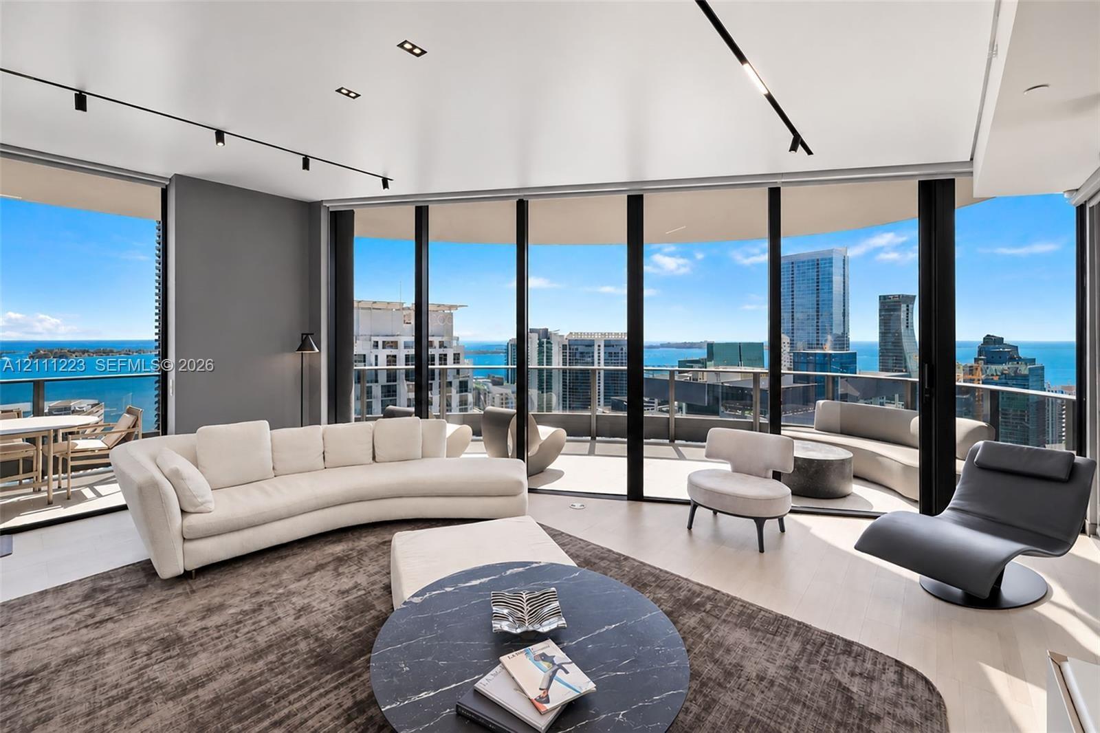 Floor-to-ceiling glass walls, expansive wrap-around balcony, light-toned wood-finish flooring, and industrial-style track lighting