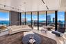 Floor-to-ceiling glass walls, curved balcony with railing, light-tone flooring, recessed track lighting, and panoramic urban and water scenery