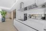 Kitchen featuring high-gloss cabinetry, a spacious island with an integrated induction cooktop, a stainless steel range hood, and a metallic backsplas