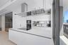 Kitchen featuring white gloss cabinetry, expansive island with integrated cooktop, stainless steel range hood, built-in wall oven, and metallic backsp