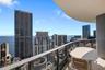 Curved private balcony with glass railing, concrete overhead covering, and panoramic urban and water scenery