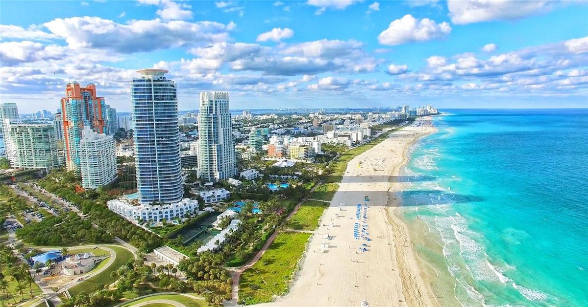 Aerial perspective of a coastal cityscape featuring high-rise buildings, extensive sand coastline, and turquoise ocean waters