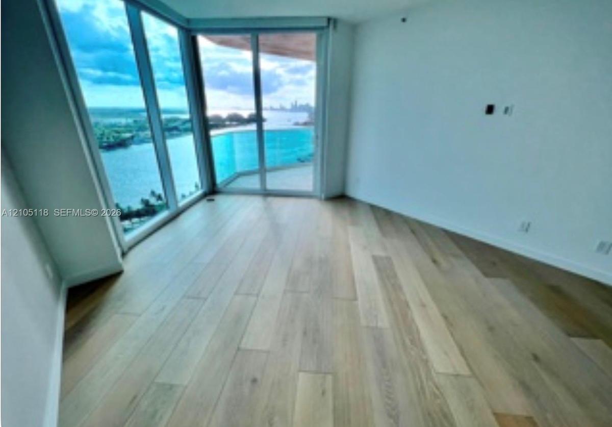 Floor-to-ceiling windows, wood-finish flooring, sliding glass door, and expansive balcony with water backdrop