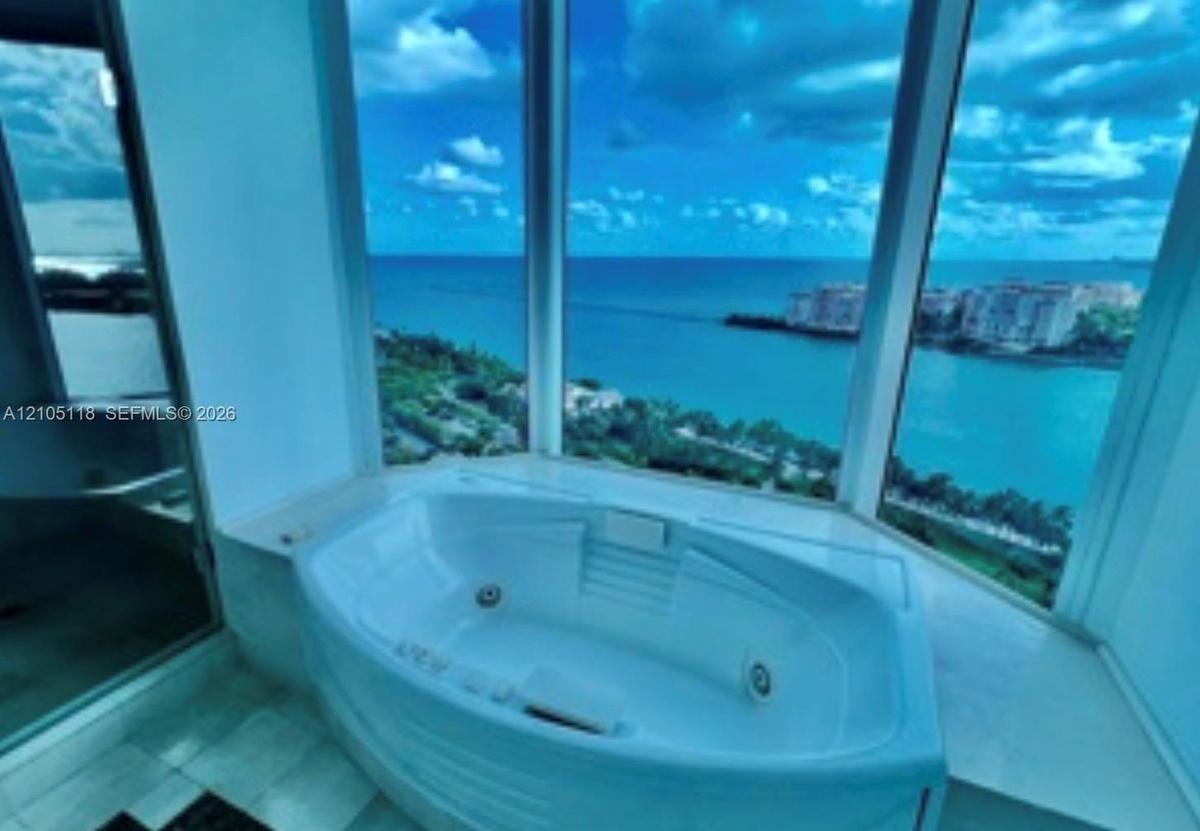 Oval soaking tub with integrated jets, expansive floor-to-ceiling windows, and tile flooring