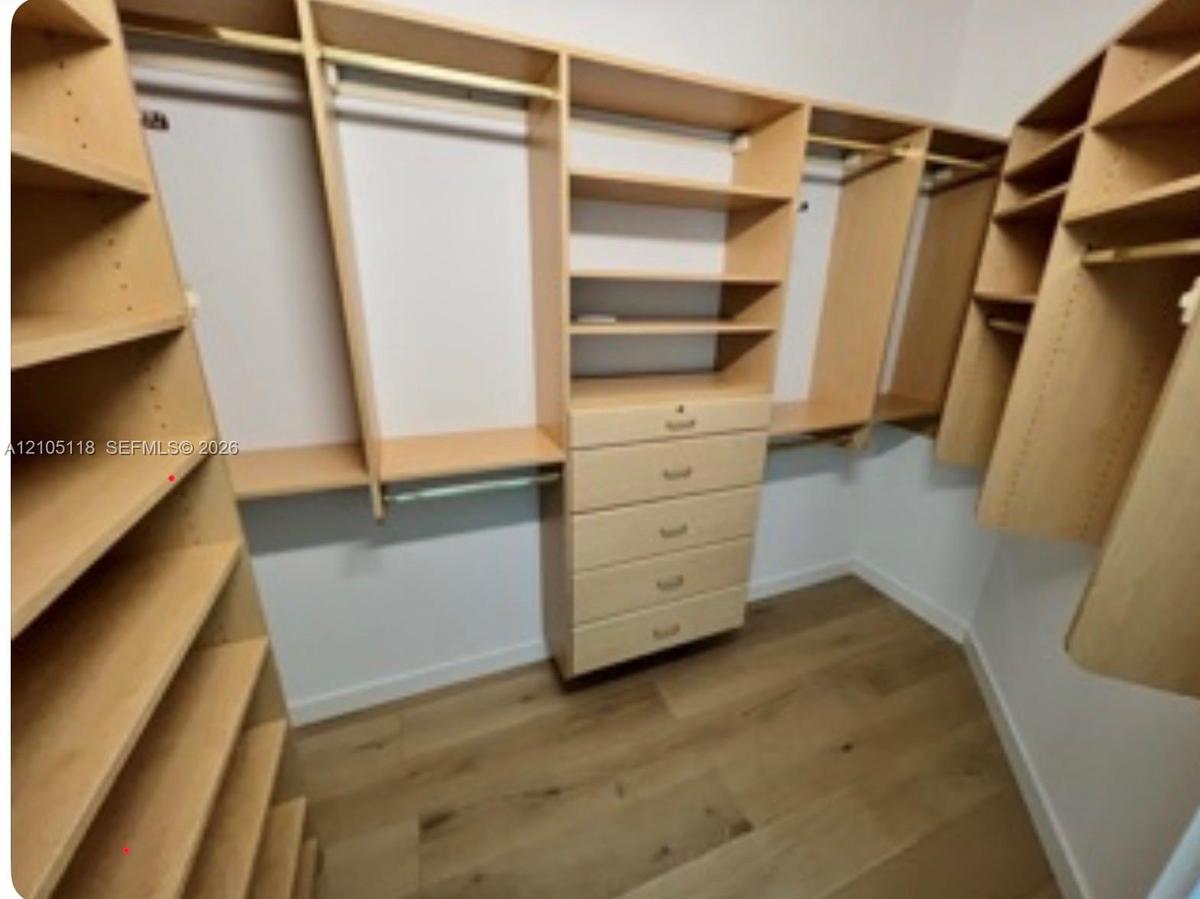 Walk-in closet featuring light-toned custom built-in cabinetry, multiple adjustable shelving units, integrated hanging rods, a five-drawer dresser, an