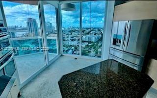 Floor-to-ceiling glass windows, stainless steel appliances, stone-surface kitchen island, and glass-railing balcony