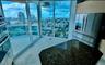 Floor-to-ceiling glass windows, stainless steel appliances, stone-surface kitchen island, and glass-railing balcony