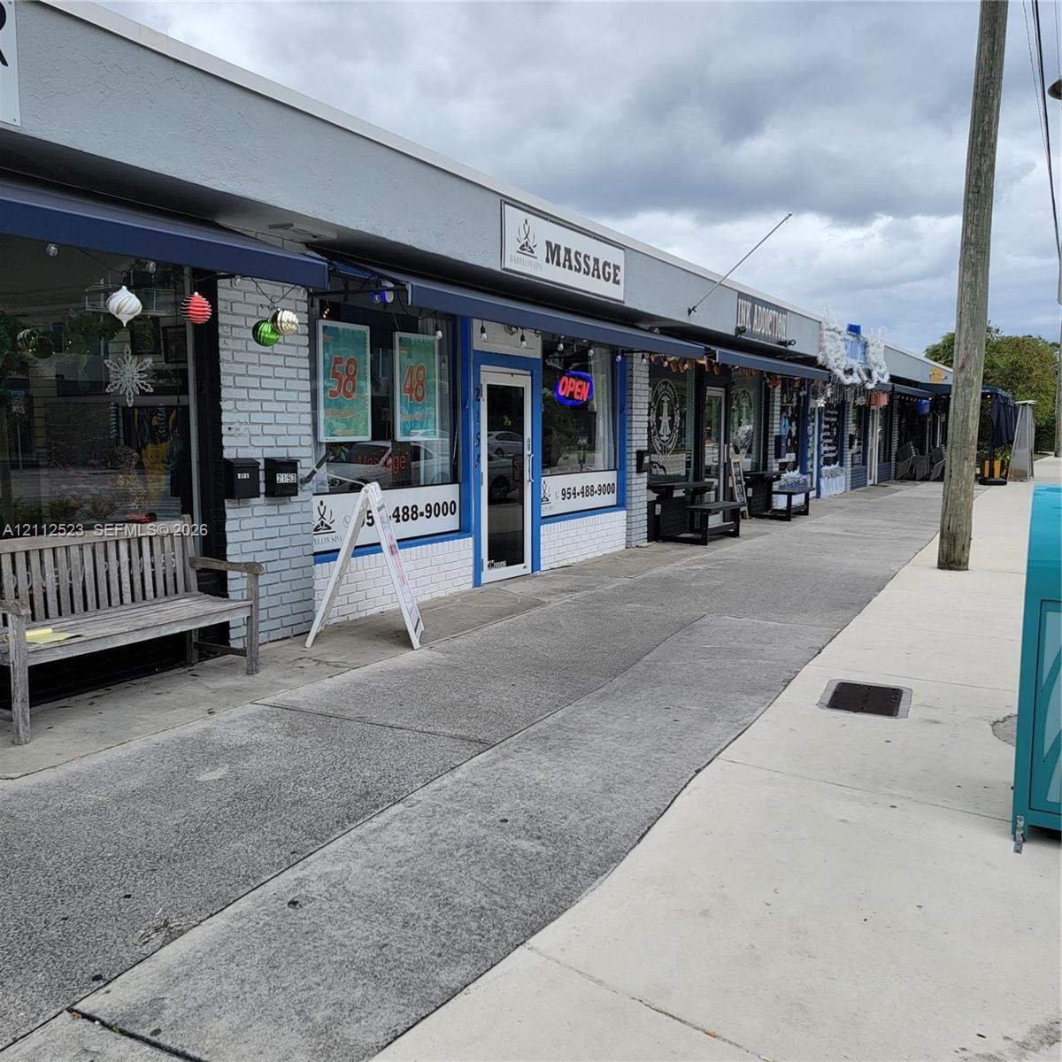 Commercial storefront exterior featuring painted brick facade, retractable fabric awnings, large glass storefront windows, and concrete sidewalk acces