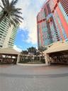 Multi-story high-rise building with a glass facade, circular paver driveway, covered porte-cochère, and a central landscaped courtyard featuring matur