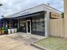 Commercial storefront featuring floor-to-ceiling glass display windows, a recessed glass entry door, an exterior retractable awning, and textured maso