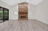Vaulted ceiling, floor-to-ceiling brick fireplace with a wood mantel, wood-finish flooring, and arched windows with interior shutters