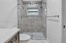 Walk-in shower featuring a sliding glass door, patterned wall tiling, hexagon mosaic floor tiling, dual shower heads, and an integrated window