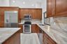Kitchen featuring wood cabinetry, natural stone countertops and backsplash, stainless steel appliances, and wood-finish flooring