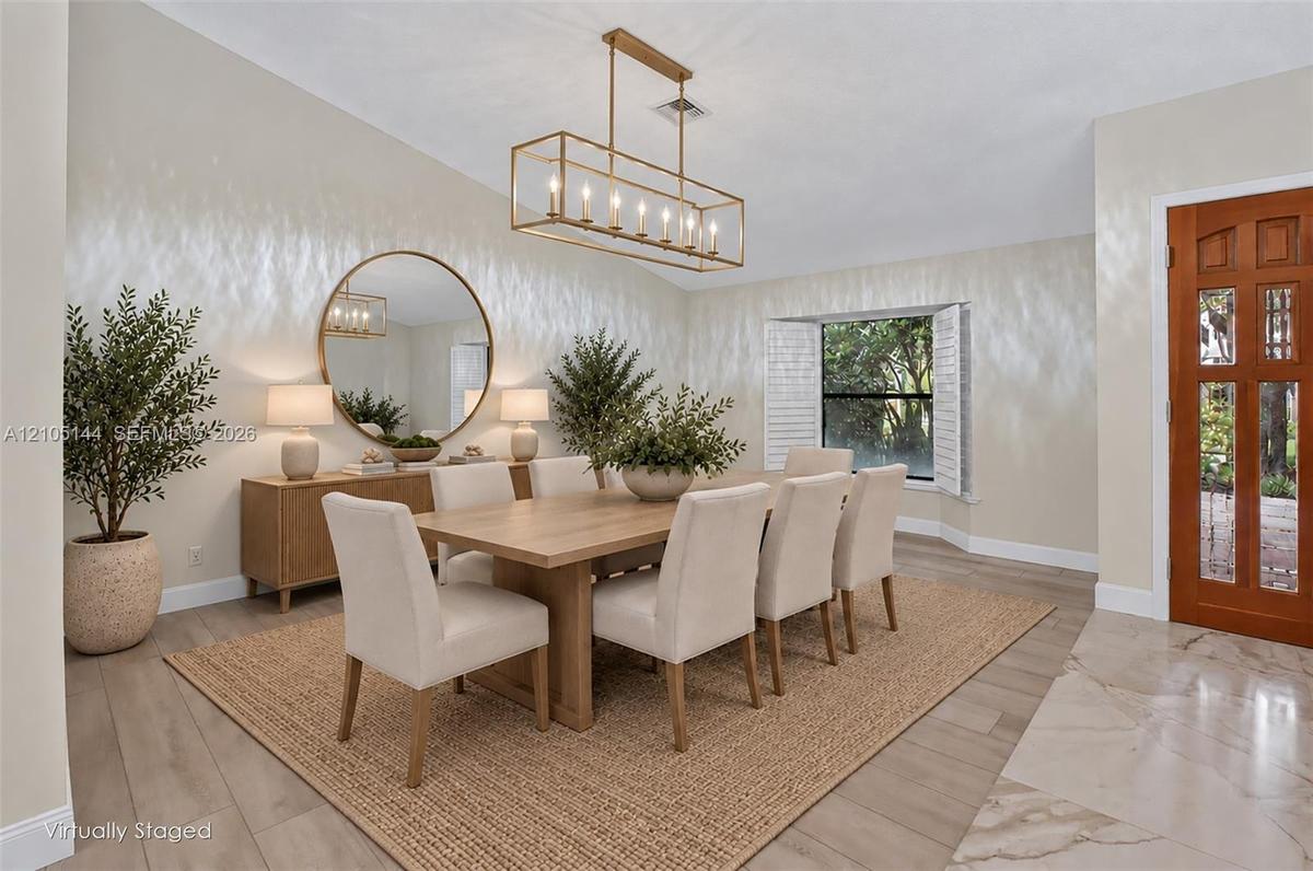 Dining room featuring wood-finish flooring, a contemporary rectangular chandelier, a large round wall mirror, and a wood-paneled door with glass inser