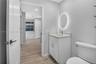 Bathroom featuring a vanity with shaker-style cabinetry, light-toned stone-finish countertop, oval backlit mirror, and wood-finish flooring