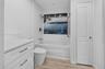 Bathroom featuring white cabinetry with stone-finish countertop, wood-finish flooring, a built-in soaking tub, decorative wall tile inlay, and a wall-