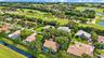 Aerial perspective of a residential neighborhood featuring golf course grounds, expansive fairway scenery, bodies of water, and mature landscaping
