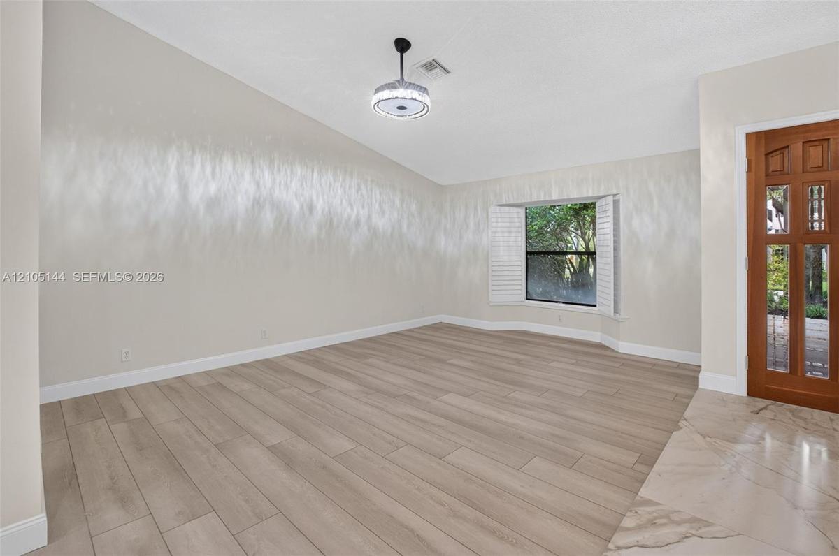 Vaulted ceilings, wood-finish flooring, recessed bay window with plantation shutters, integrated circular flush-mount lighting, and decorative wood-pa