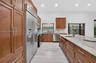 Kitchen featuring wood cabinetry, expansive stone countertops, stainless steel appliances, a center island with a prep sink, and tile flooring