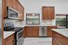 Kitchen featuring medium-tone wood cabinetry, stone-finish countertops with matching full-height backsplash, stainless steel appliances, and large-for