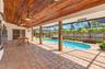 Screened-in pool area featuring a natural wood-plank ceiling, exposed brick columns, and patterned paver patio flooring