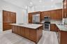 Kitchen featuring wood cabinetry, large central island, stone countertops, stainless steel appliances, and wood-finish flooring