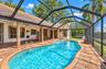 Screen-enclosed patio area featuring a free-form swimming pool, brick-paver decking, covered lanai with exposed brick columns, and a built-in spa
