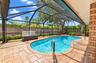 Screened-in pool area featuring a paver deck, brick siding, built-in wooden planters, and a wood privacy fence