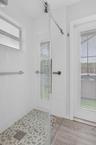 Walk-in shower featuring a sliding glass door, hexagonal tile flooring, wall-mounted brushed metal hardware, and a rainfall shower head