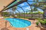 Screened pool enclosure featuring paver decking, stainless steel pool ladder, and wood privacy fencing