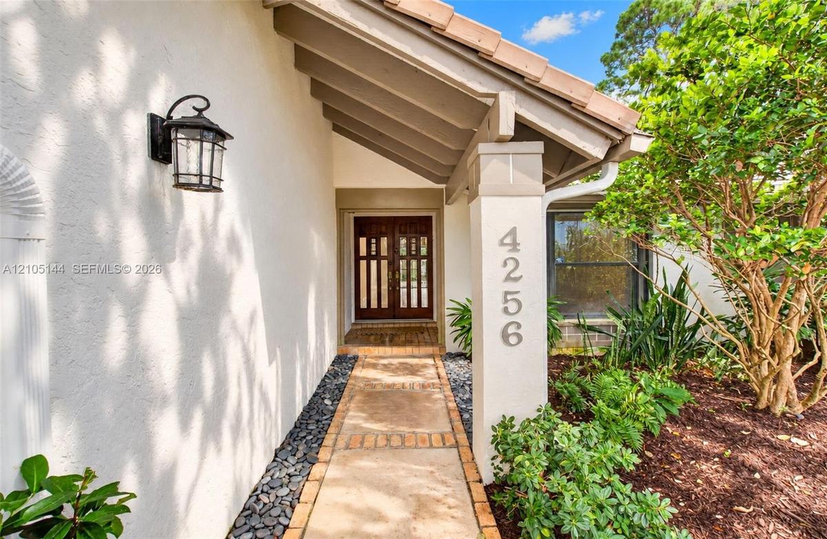 Covered entryway featuring a concrete paver walkway, stucco exterior, decorative wall-mounted light fixture, and double entry doors with vertical glas