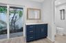 Navy blue vanity with light-toned stone countertop, integrated rectangular sink, framed mirror, and sliding glass door with external patio access