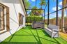Screened lanai featuring synthetic grass flooring, a built-in hot tub, and a wood-tone fence enclosure