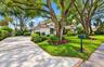 Stucco exterior residence featuring a concrete driveway with brick paver borders, mature canopy trees, and landscaped garden beds