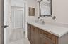 Vanity featuring a stone-composite countertop, undermount sink, shaker-style cabinetry with polished hardware, wall-mounted metallic mirror, and built