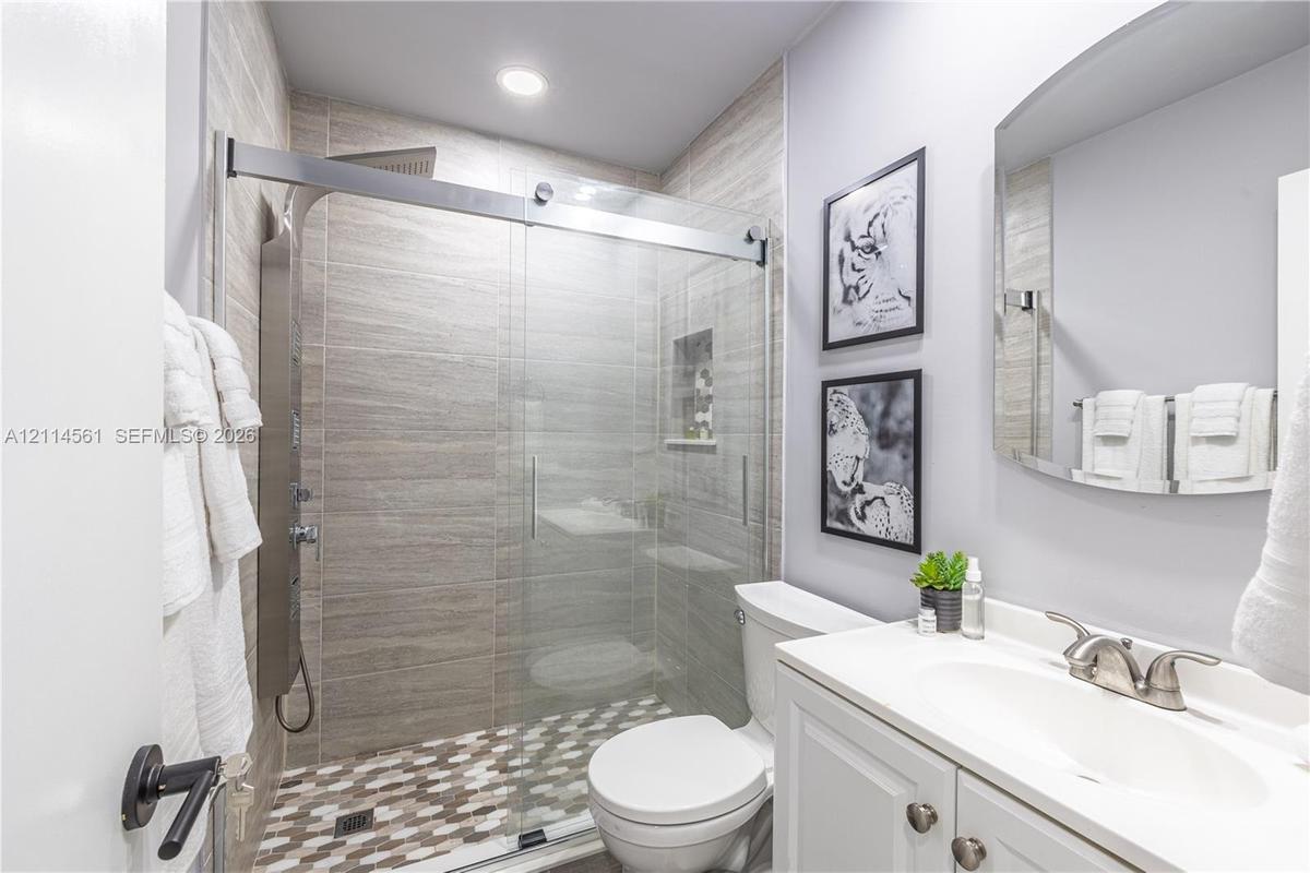 Bathroom featuring a glass-enclosed shower with horizontal wall tile, mosaic floor tiling, built-in recessed shelving, a multi-function shower panel, 
