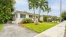 Stucco exterior residence featuring a tiled roof, concrete driveway, mature palm trees, and manicured landscaping