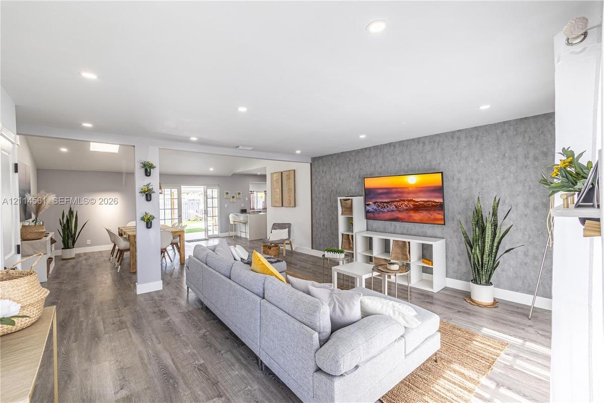 Open-concept living space featuring wood-finish flooring, recessed lighting, and a textured accent wall