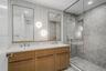 Dual-sink vanity with fluted wood-finish cabinetry, rectangular under-mount basins, wall-mounted round lighting, and a glass-enclosed shower featuring