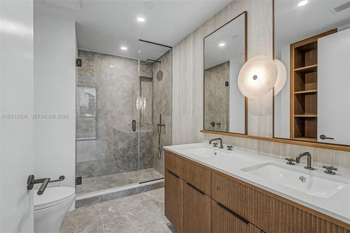 Double vanity featuring wood-finish cabinetry, white countertop, integrated sinks, and dual mirrors