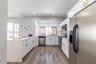 Kitchen featuring white cabinetry with gold-tone hardware, stone-finish countertops, stainless steel appliances, and wood-finish flooring