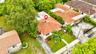 Aerial view featuring a residence with a clay tile roof, white stucco exterior, prominent chimney, and surrounding mature landscaping