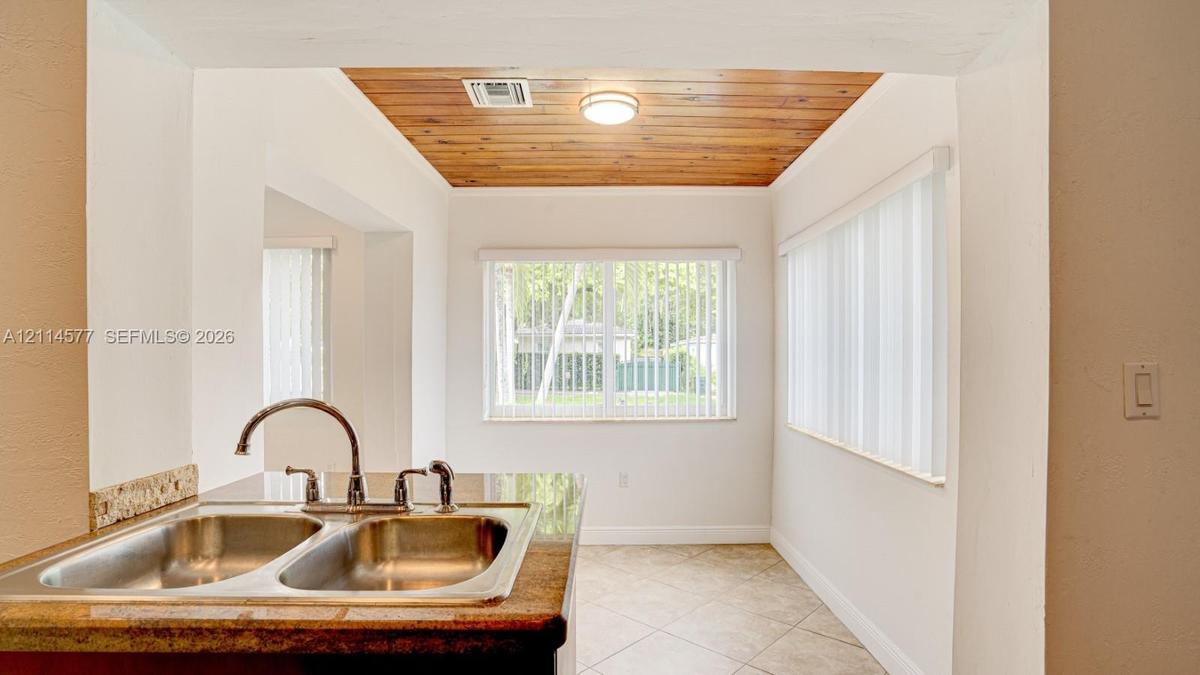 Double-basin stainless steel sink with high-arc faucet, stone-surfaced countertop, natural wood-paneled ceiling, and ceramic tile flooring