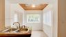 Double-basin stainless steel sink with high-arc faucet, stone-surfaced countertop, natural wood-paneled ceiling, and ceramic tile flooring