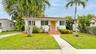 Stucco exterior with a tile roof, natural wood-finish front door, terracotta tiled entry steps, wrought iron handrails, and mature palm landscaping