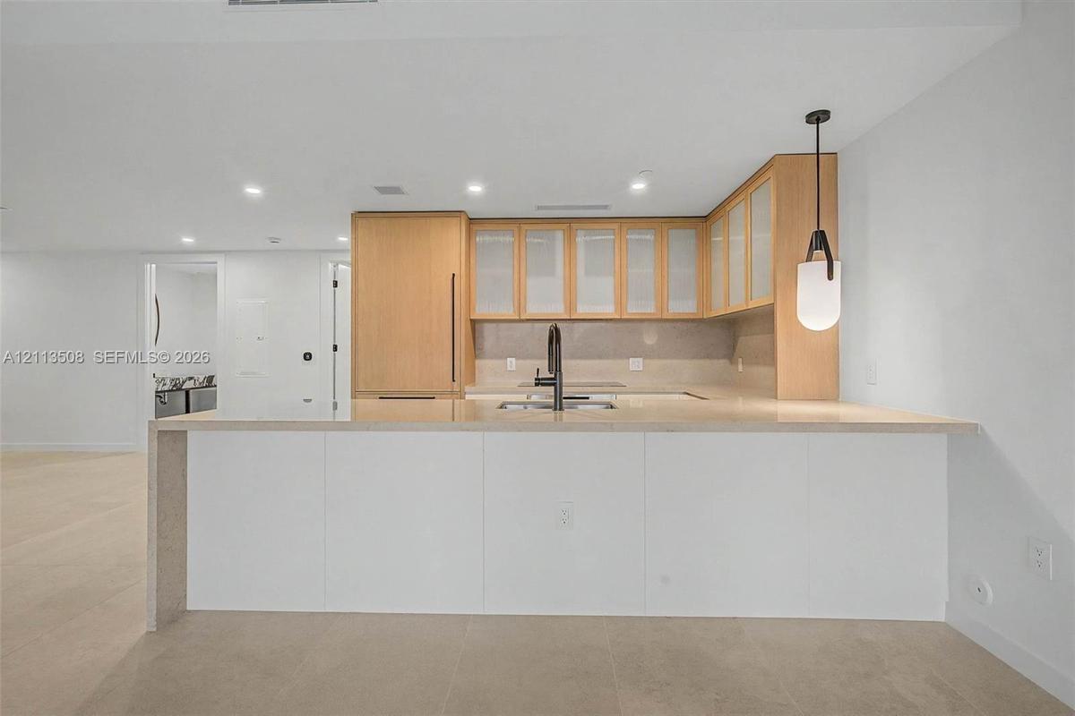 Kitchen featuring wood cabinetry with glass-panel upper doors, a stone-finish waterfall edge island, a matte black high-arch faucet, integrated applia